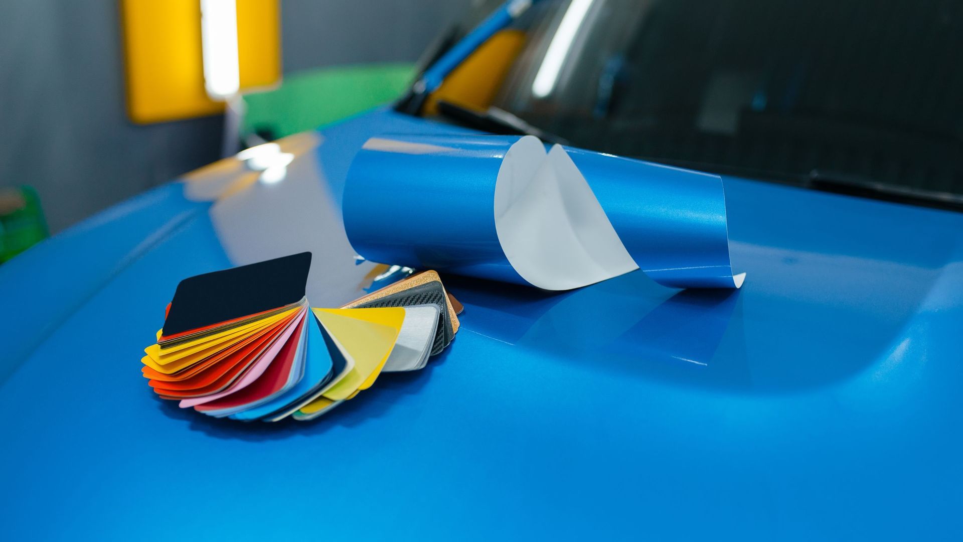Blue car hood with color swatches and a roll of blue wrap, showing car wrapping options.