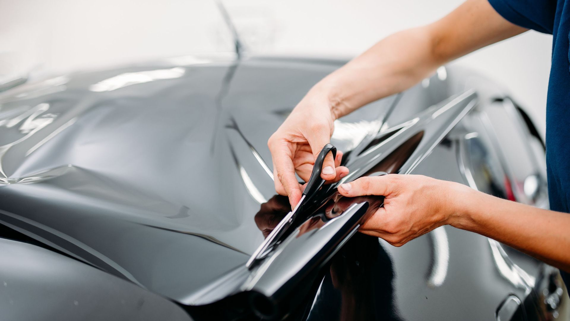 Person using scissors to trim window tint film on a car's rear window.