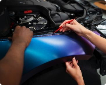 Two people applying blue and purple car wrap to a vehicle's fender.