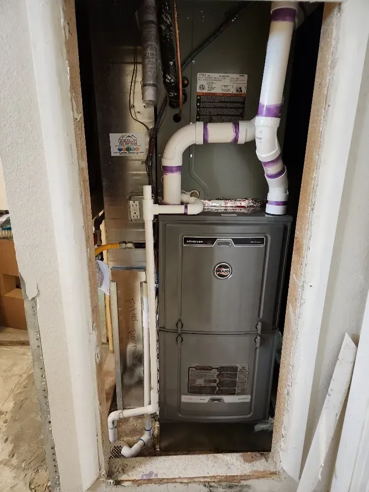 A furnace is sitting in a closet with pipes coming out of it.
