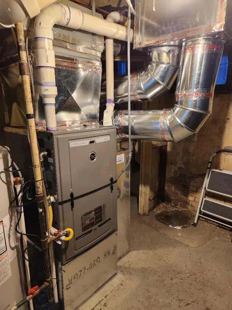 A furnace is sitting in a basement next to a ladder.