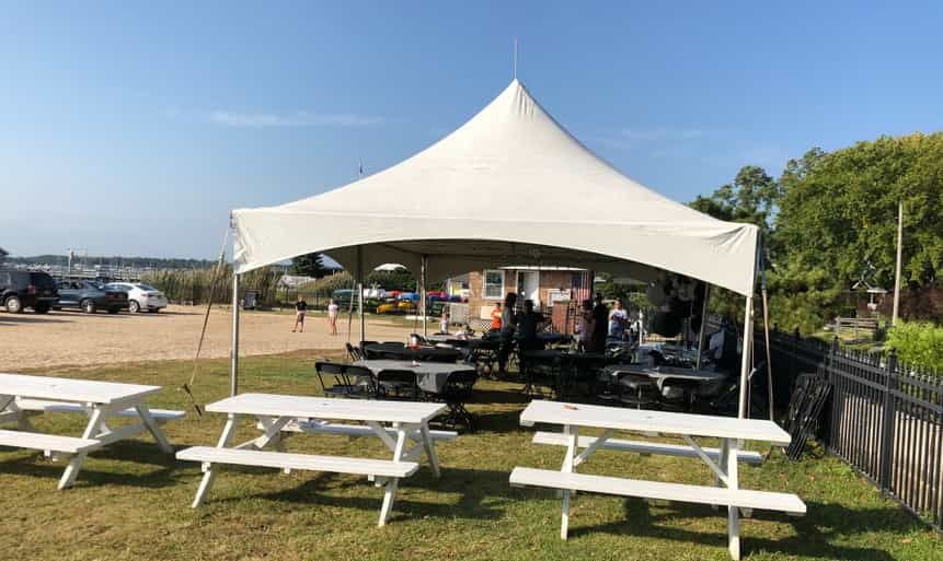 A group of white picnic tables under a white tent.