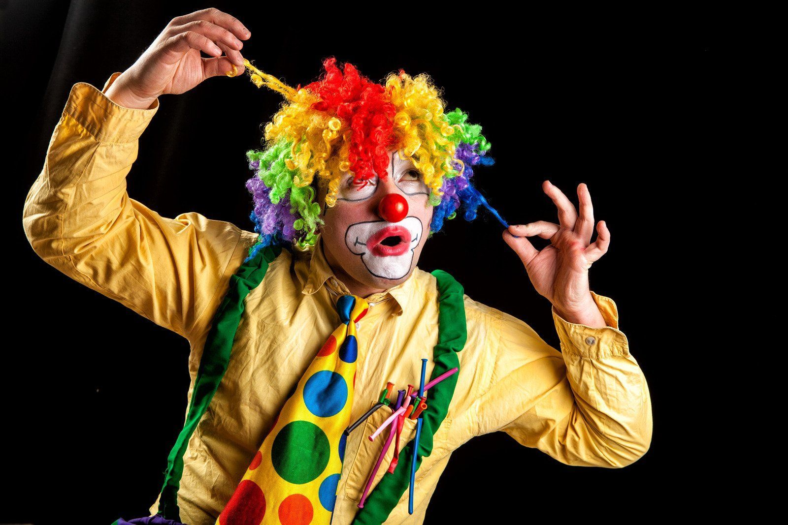 A man dressed as a clown is holding a balloon in his hand.
