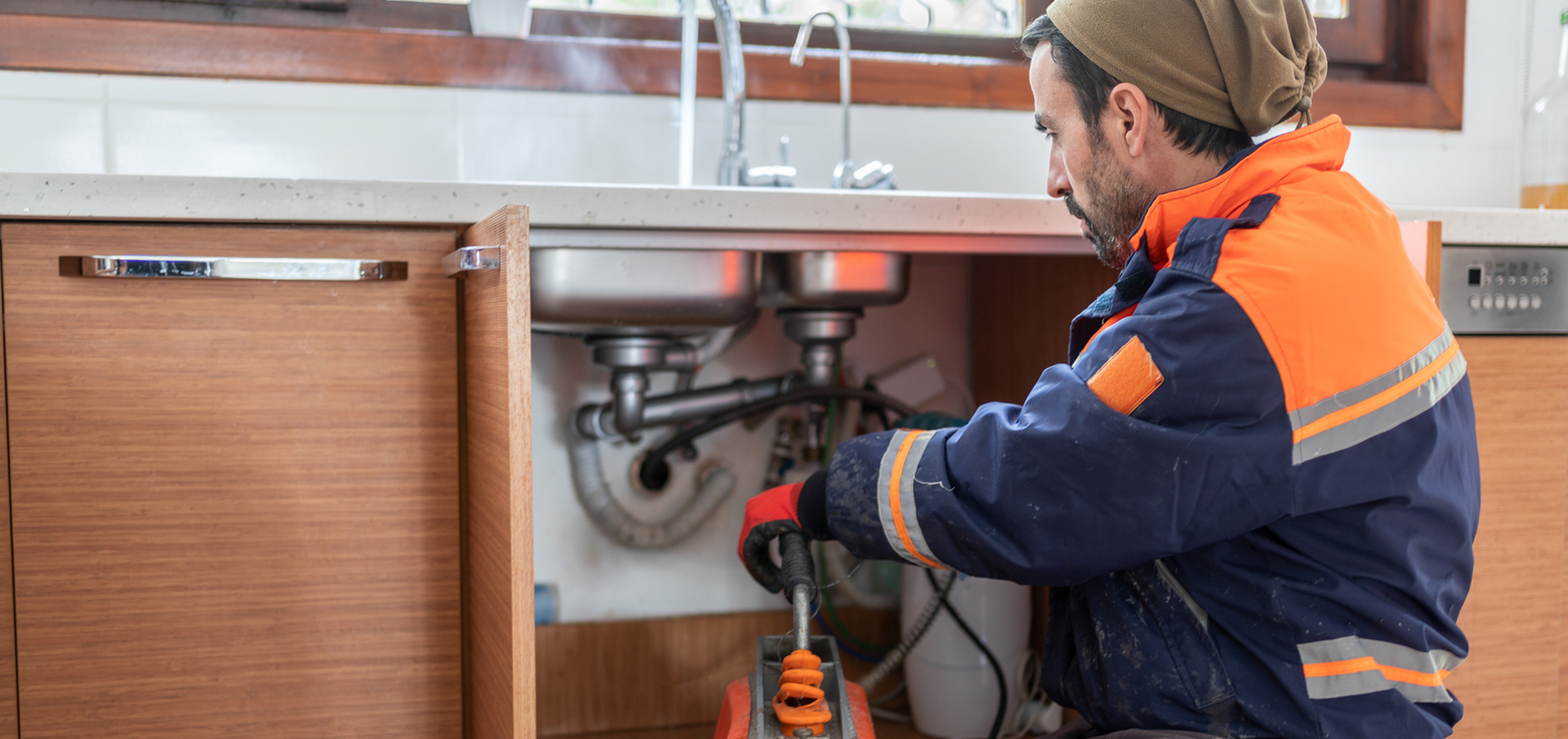 A plumber is fixing a sink in a kitchen.