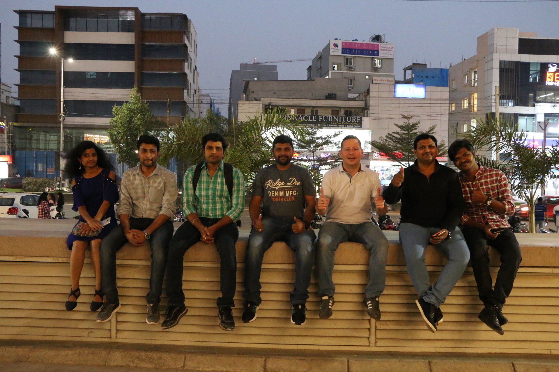 A group of people are sitting on a wall in front of a city.