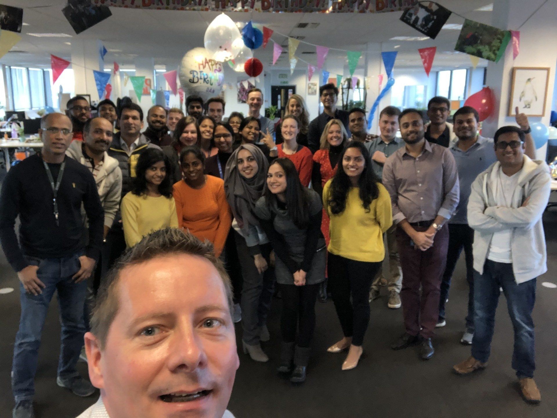 A group of people are posing for a picture in a room with balloons hanging from the ceiling.