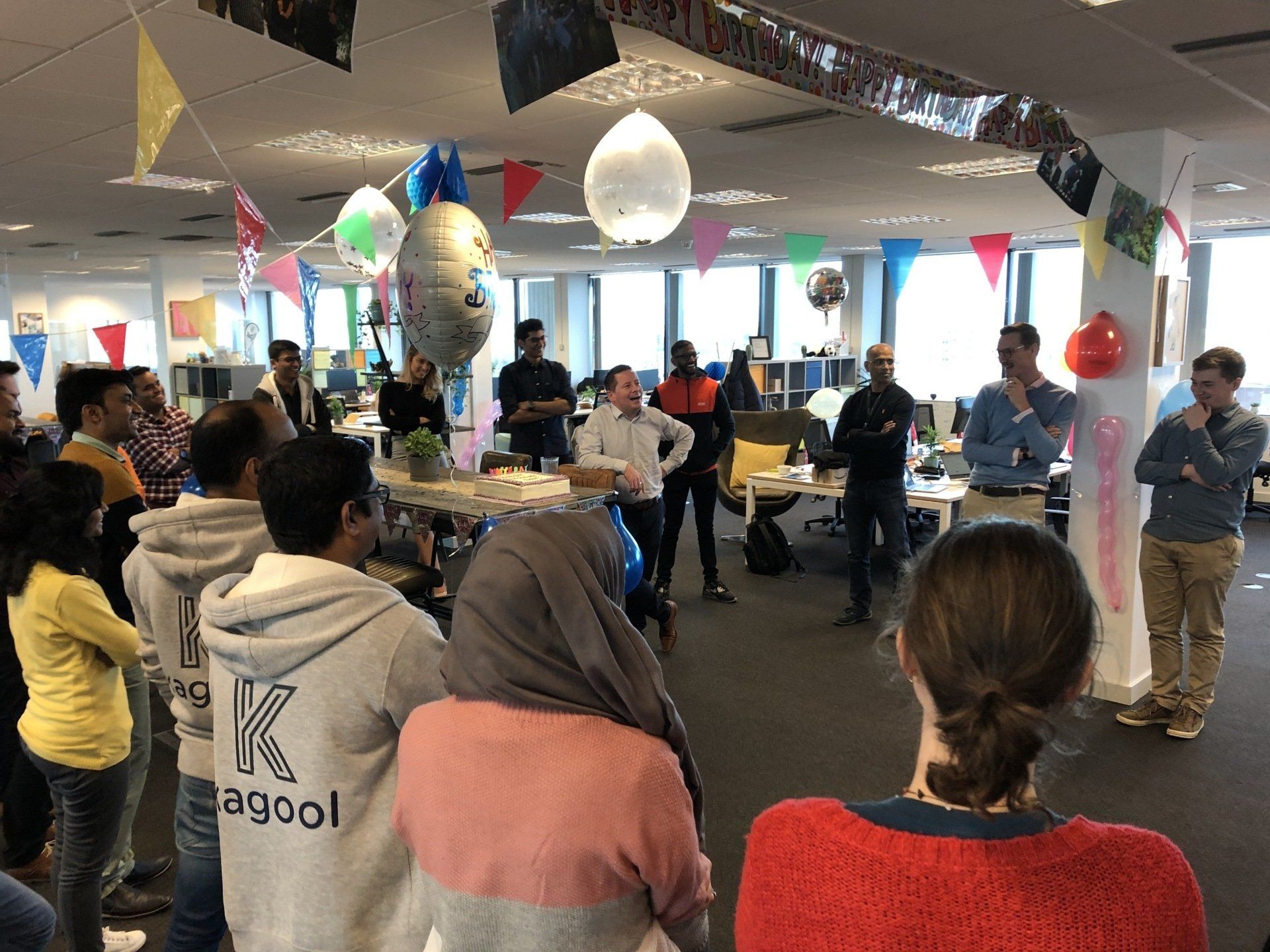 A group of people are standing in a room with balloons hanging from the ceiling.