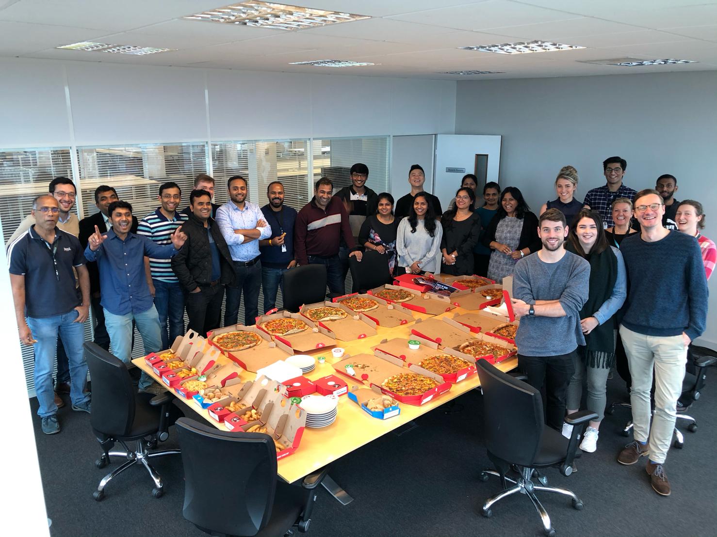 A group of people are standing around a table with pizza on it.
