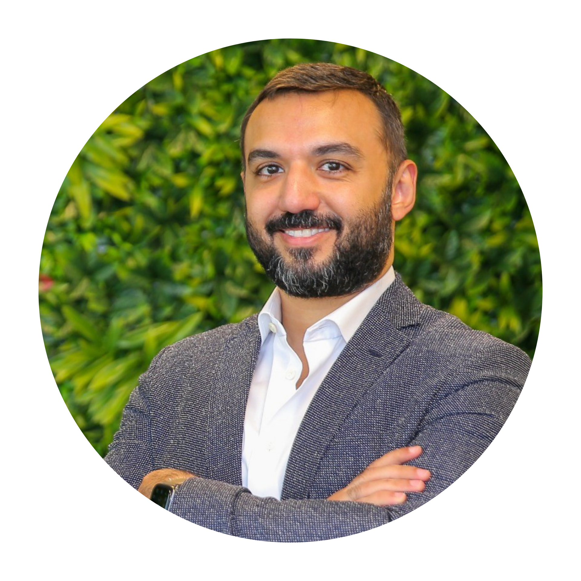 A man with a beard is smiling with his arms crossed in front of a green wall.