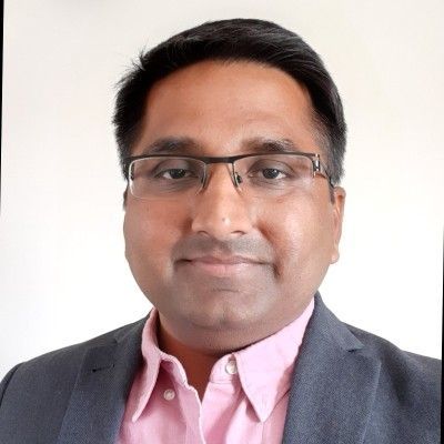 A bald man wearing glasses and a blue shirt is smiling