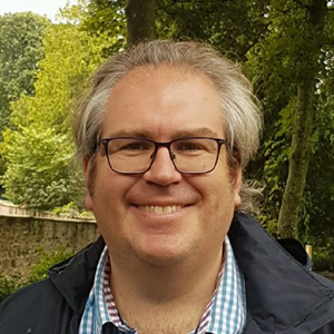 A man wearing glasses and a plaid shirt is smiling for the camera.