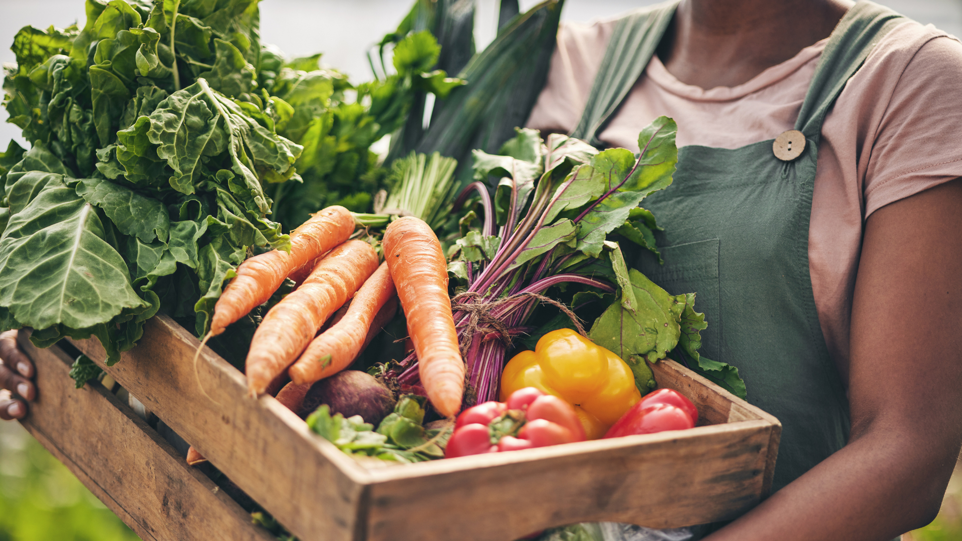 A woman is holding a wooden box filled with fresh vegetables.