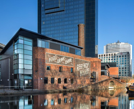 A large brick building with a chimney is next to a body of water.