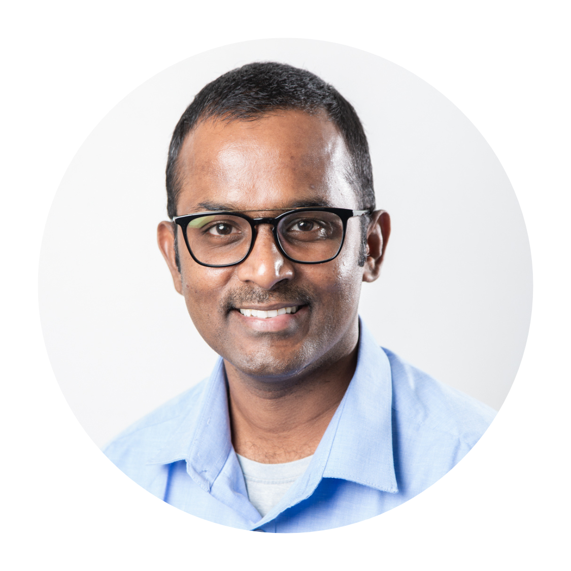 A man wearing glasses and a blue shirt is smiling for the camera.