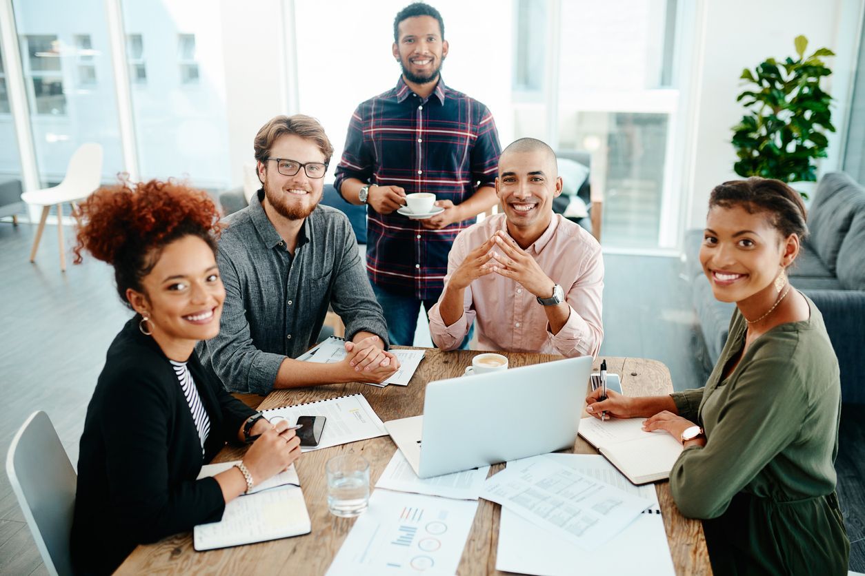 A group of people are sitting around a table with laptops.