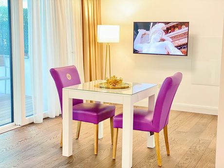 A dining room table with purple chairs and a flat screen tv on the wall.