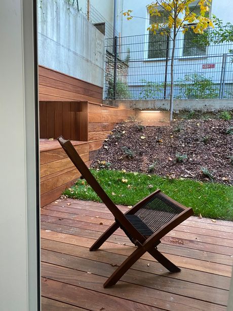 A wooden chair is sitting on a wooden deck next to a window.