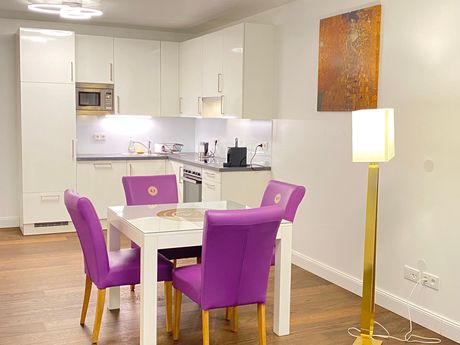 A dining room table with purple chairs in front of a kitchen.