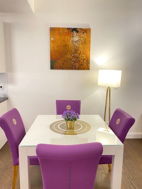 A dining room table with purple chairs and a painting on the wall above it