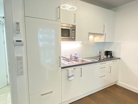 A kitchen with white cabinets , a sink , a microwave and a refrigerator.