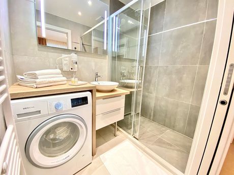 A bathroom with a washing machine , sink and shower.