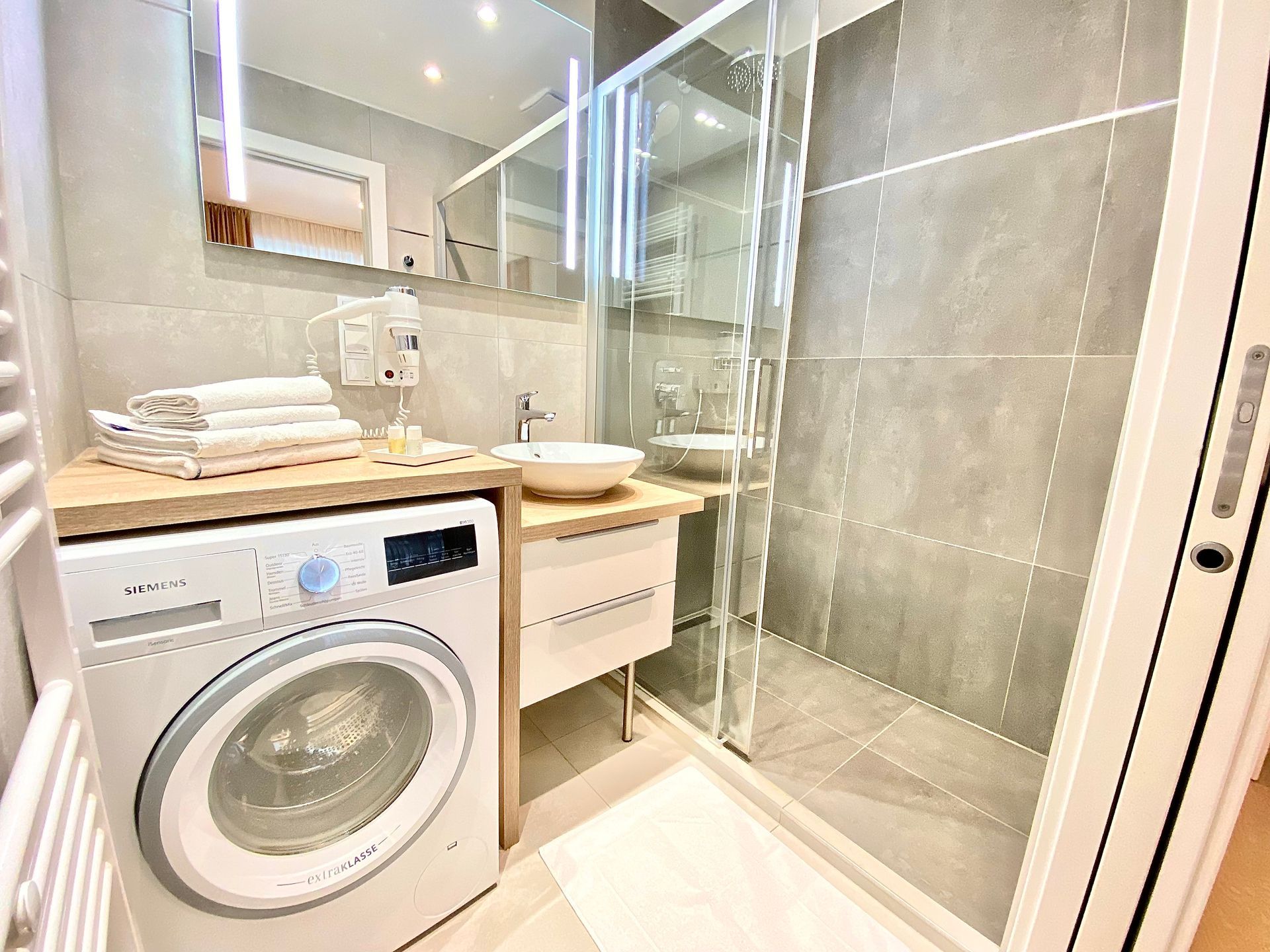 A bathroom with a washing machine , sink and shower.