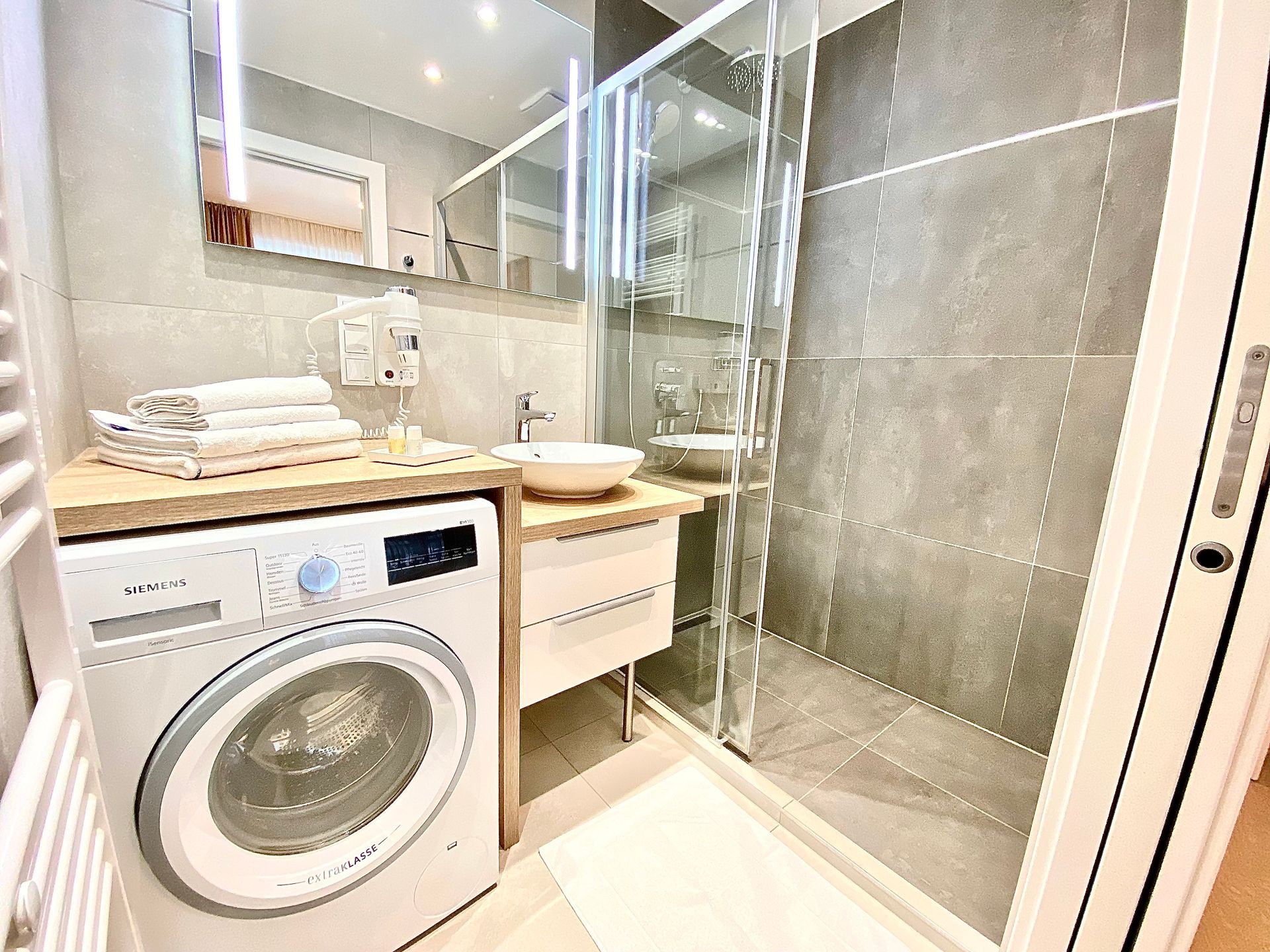 A bathroom with a washing machine , sink and shower.