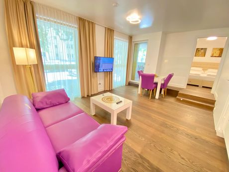 A living room with a purple couch , table , chairs and television.