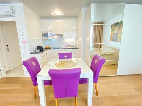 A dining room table with purple chairs and a kitchen in the background.