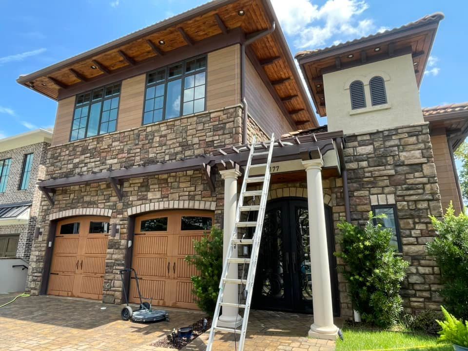 Two-story house with stone facade, brown garage doors, and a ladder leaning against the front.