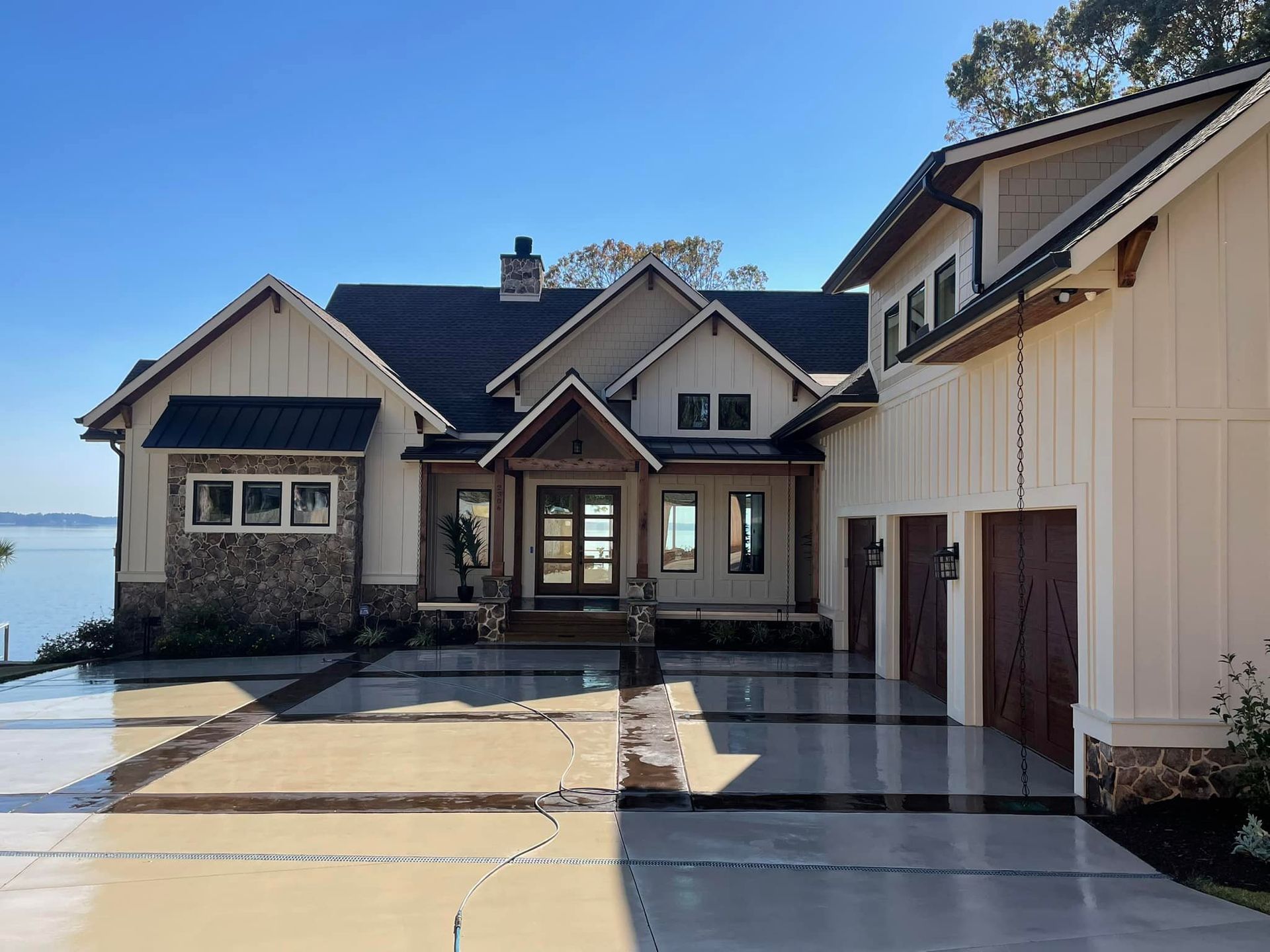 Luxurious modern house with stone and wood accents, overlooking water and a paved driveway.