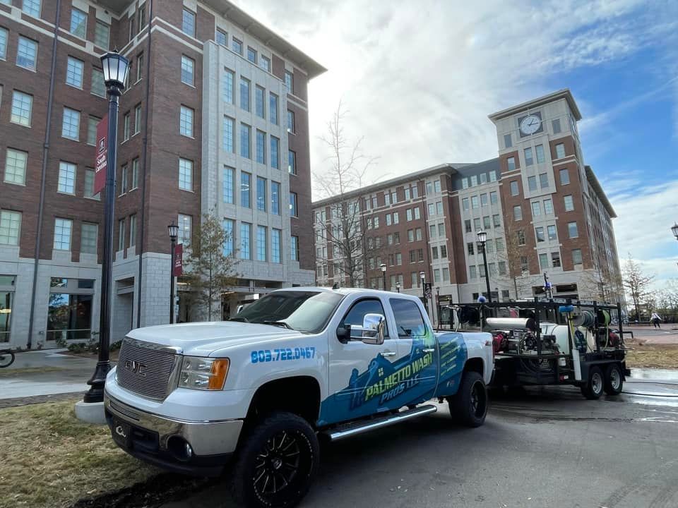 White pickup truck with trailer parked in front of brick buildings, under a cloudy sky.