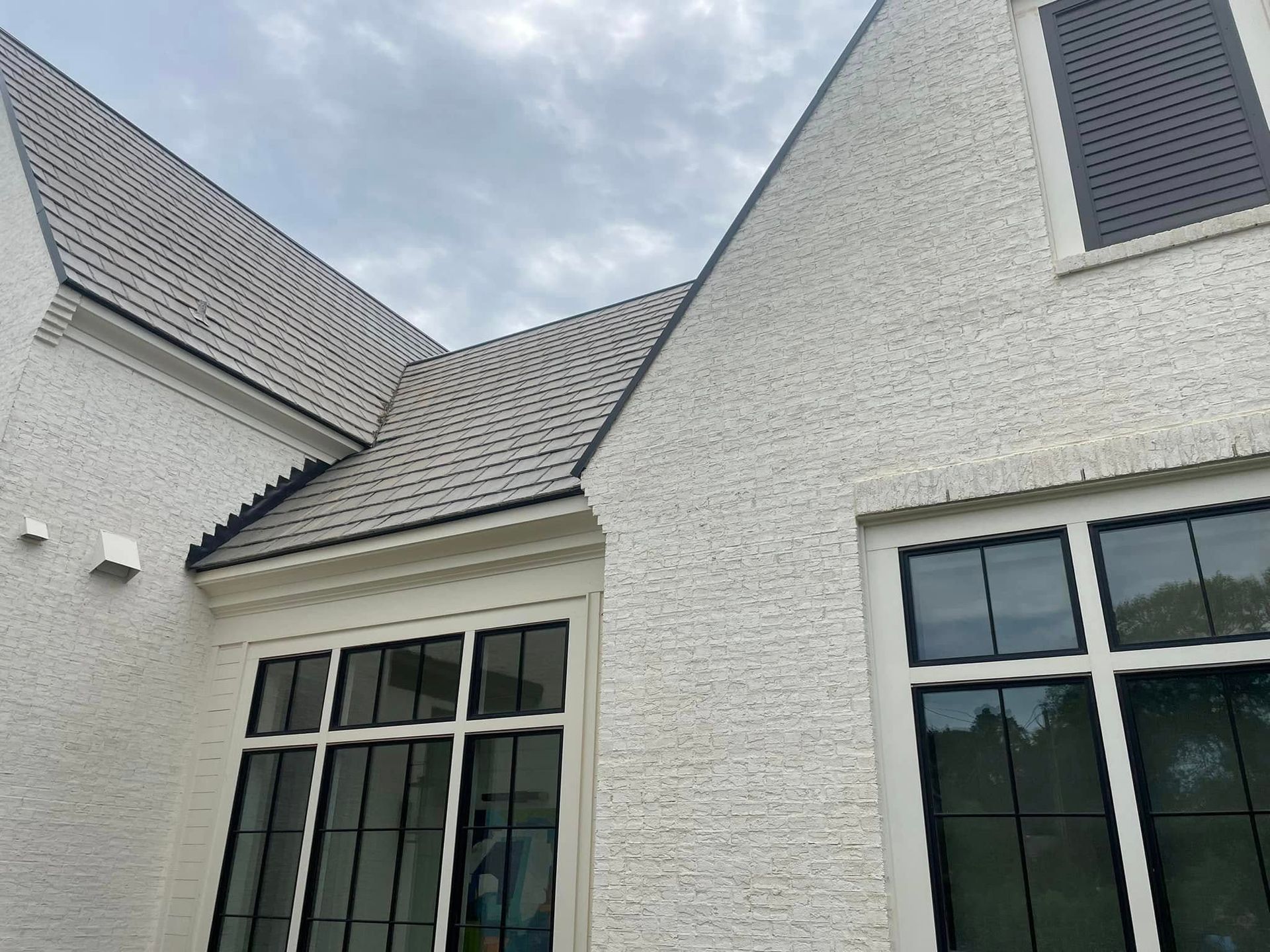 White stucco house with dark roof and black-framed windows against a cloudy sky.