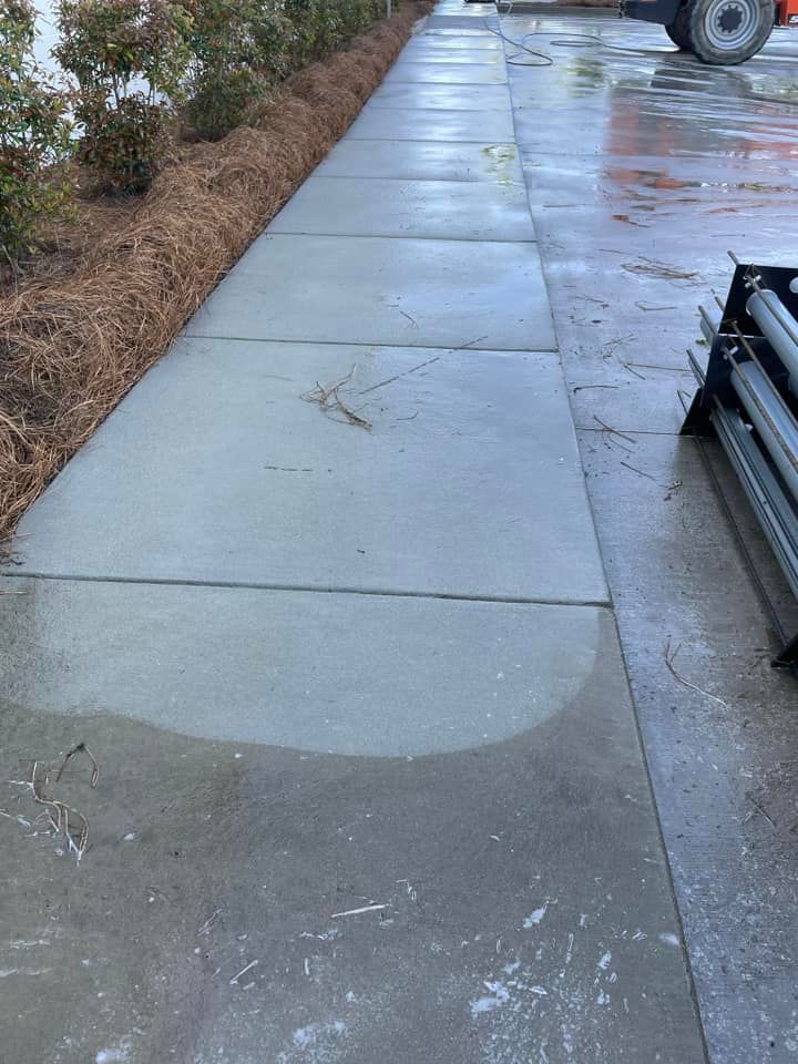 Wet concrete sidewalk with mulch and bushes on one side, metal beams on the other.