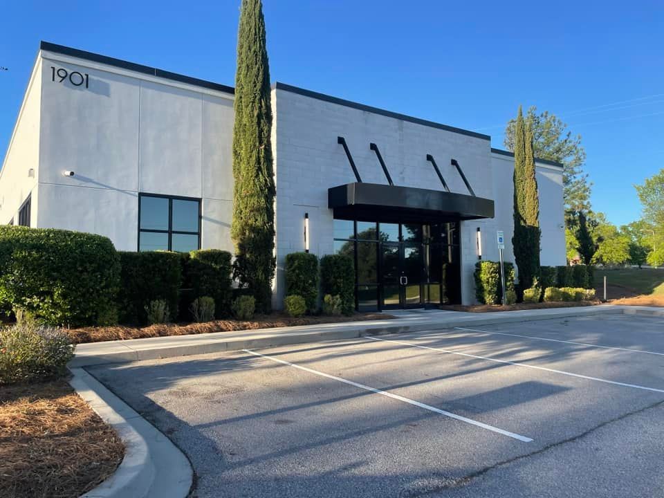 Modern commercial building with black awning, windows, and manicured landscaping.