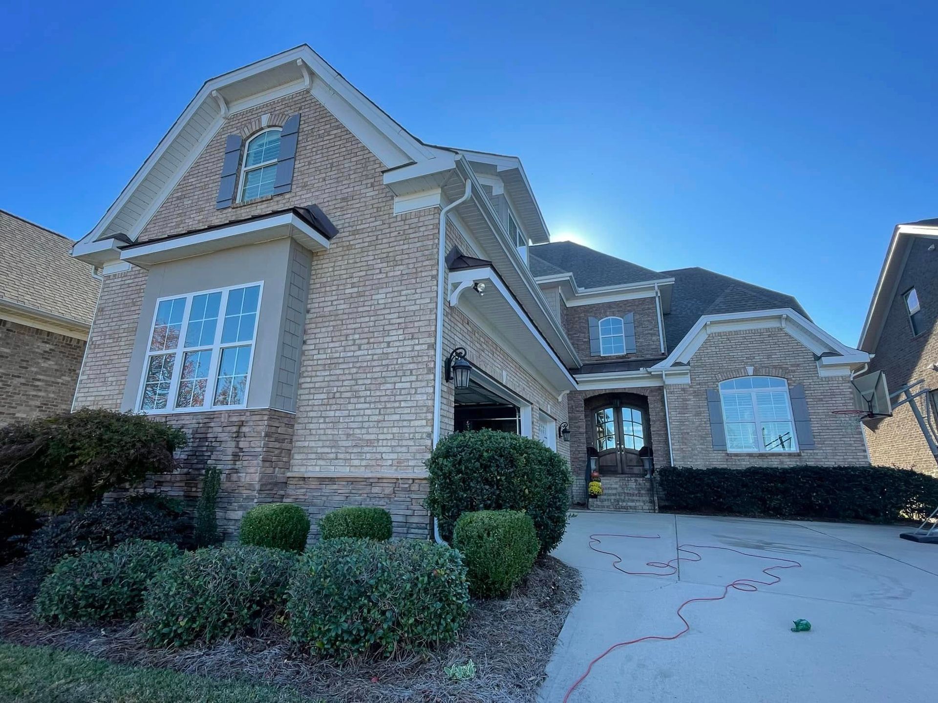 Two-story brick house with blue shutters, a garage, and a driveway on a sunny day.
