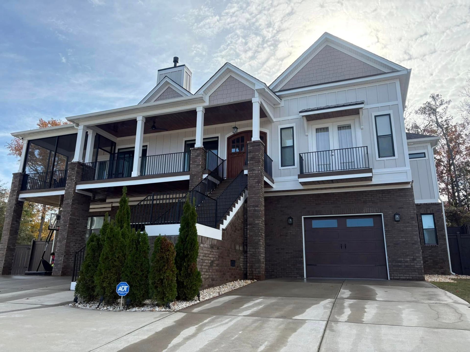 Two-story white house with brick accents, garage, and porch. Cloudy sky.