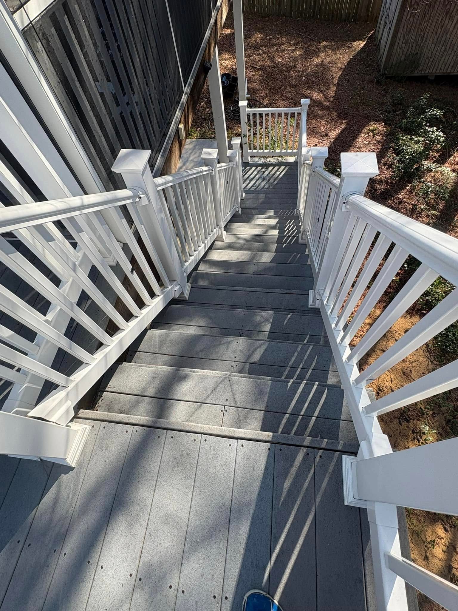 Staircase descending outdoors, gray steps, white railing, leading to a small deck area, trees in background.