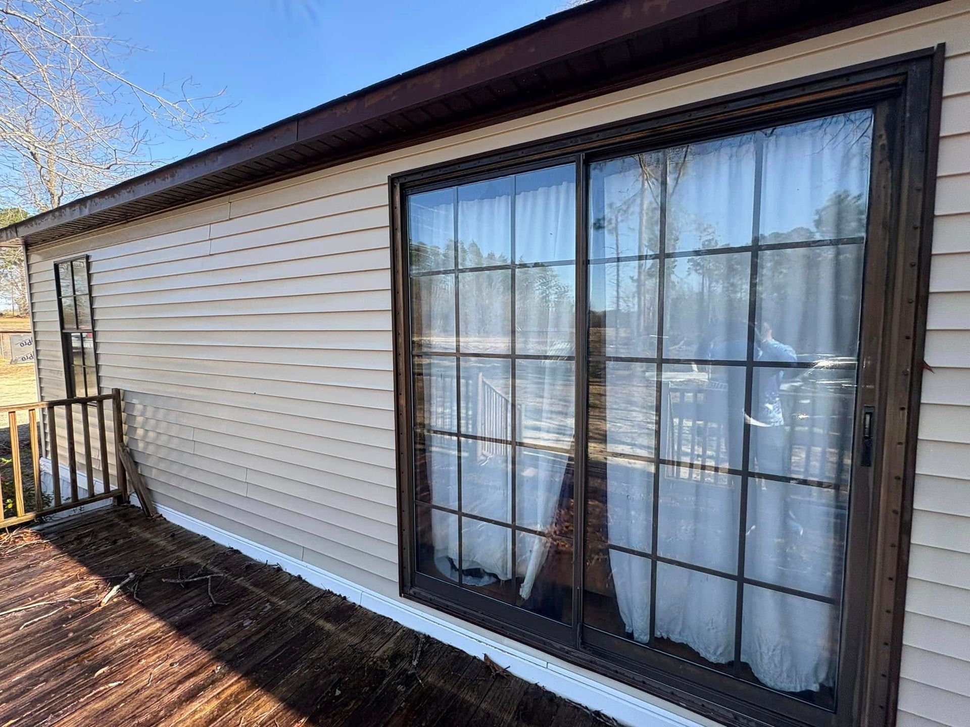 Exterior of a house with light siding and a sliding glass door. A wooden deck is in the foreground.