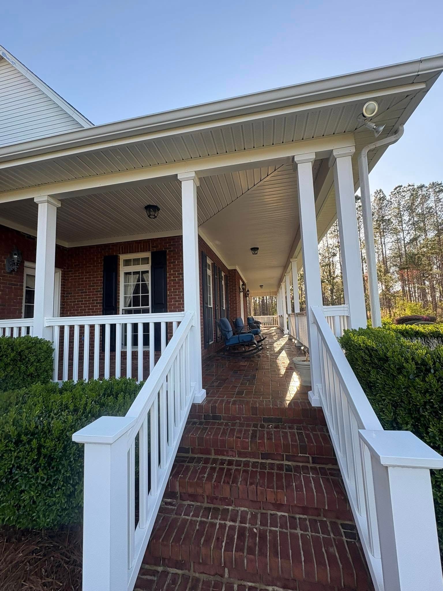 Long, covered porch with brick stairs, white railings, and brick home exterior.
