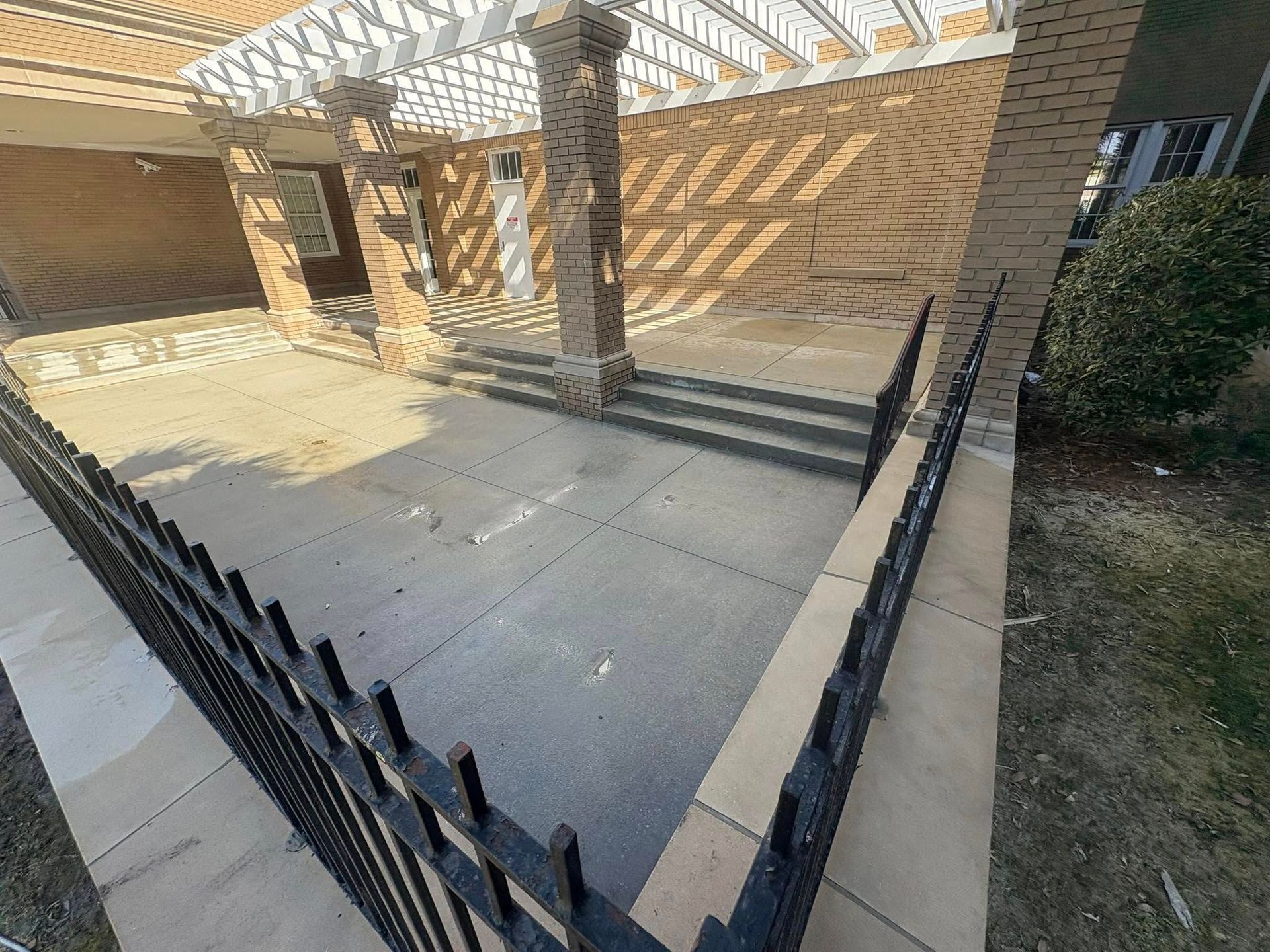 Exterior patio with black iron fence, brick columns, and a pergola overhead.