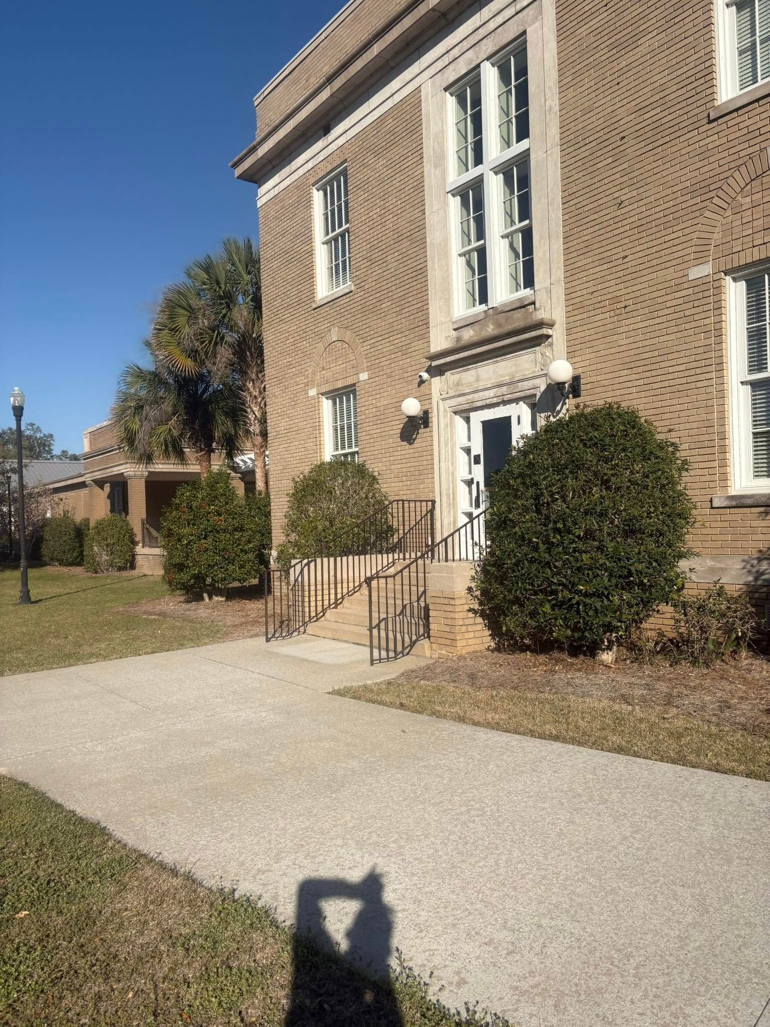 Brick building with several windows, a small set of steps, and a sidewalk on a sunny day.