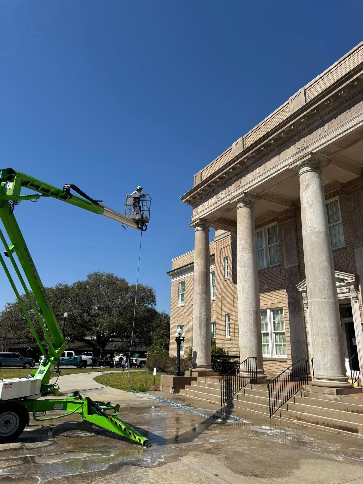 A person in a lift cleaning a building's columns and facade under a clear blue sky.