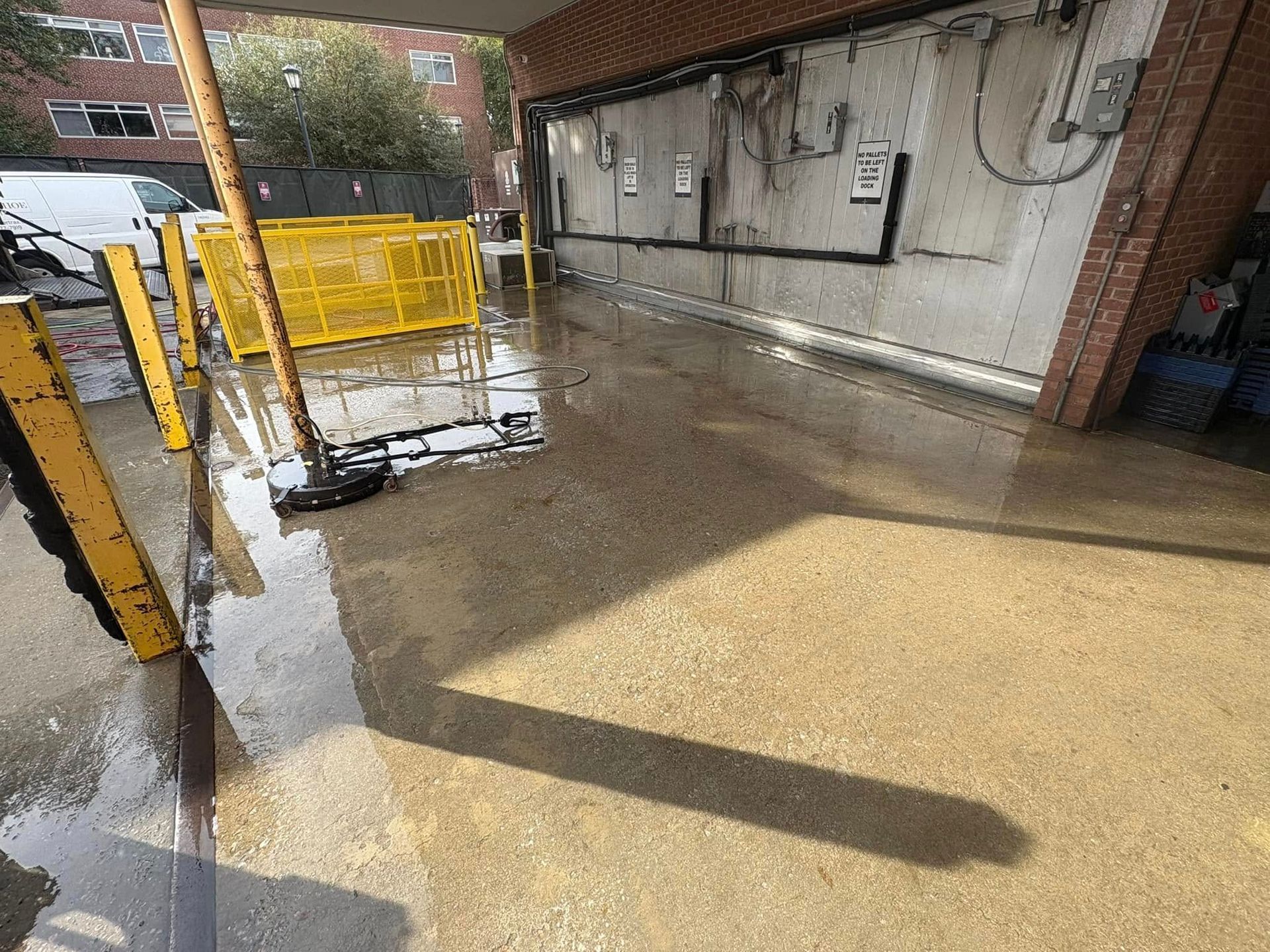 Wet, concrete loading dock area with a yellow barrier and shadows cast by sunlight.