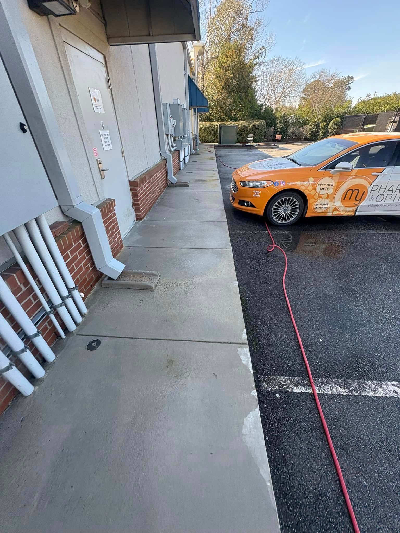 Sidewalk next to a building with conduit and orange-and-white car parked nearby.