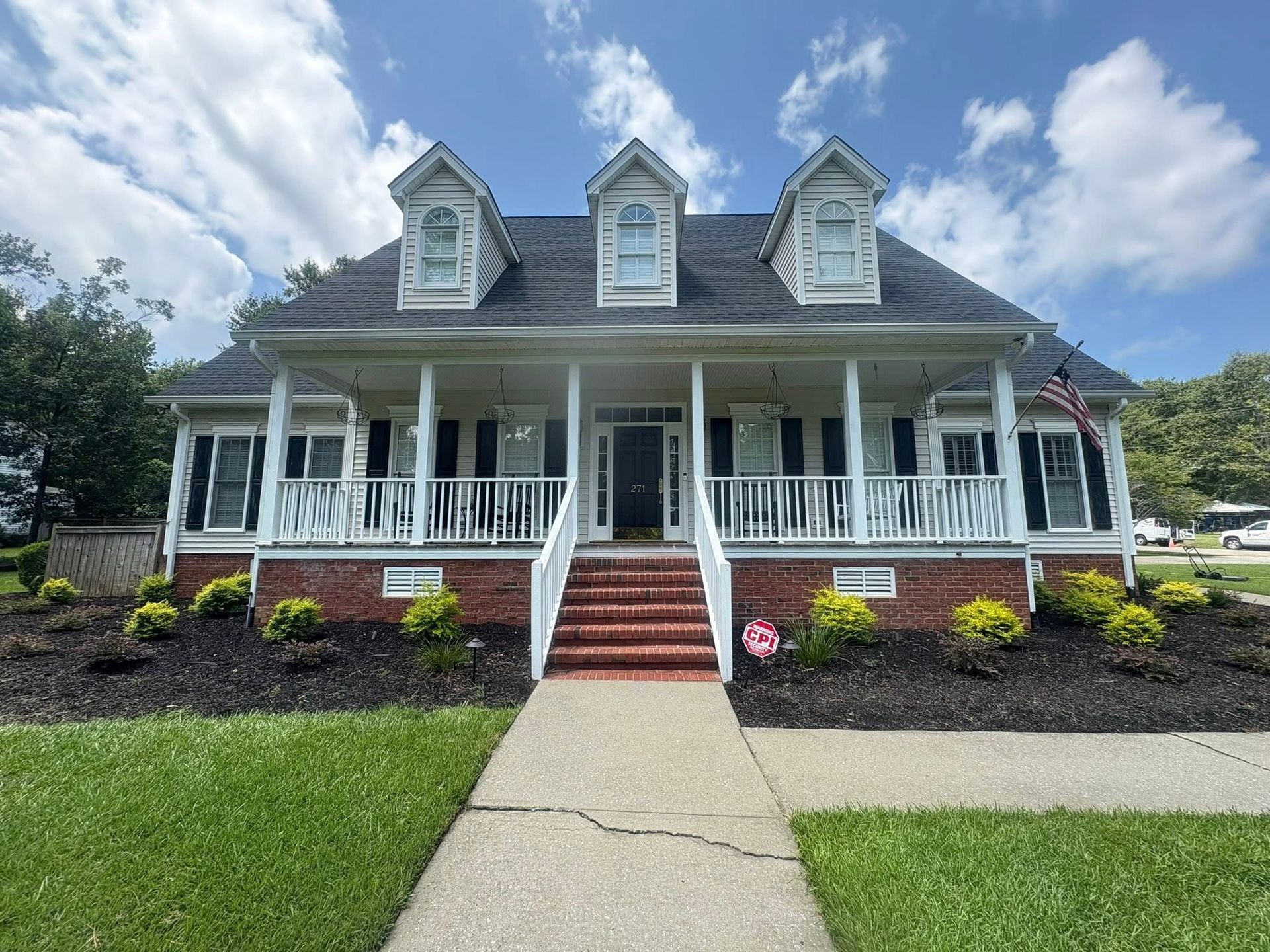 A two-story house with a porch, brick foundation, and dark roof under a cloudy sky.
