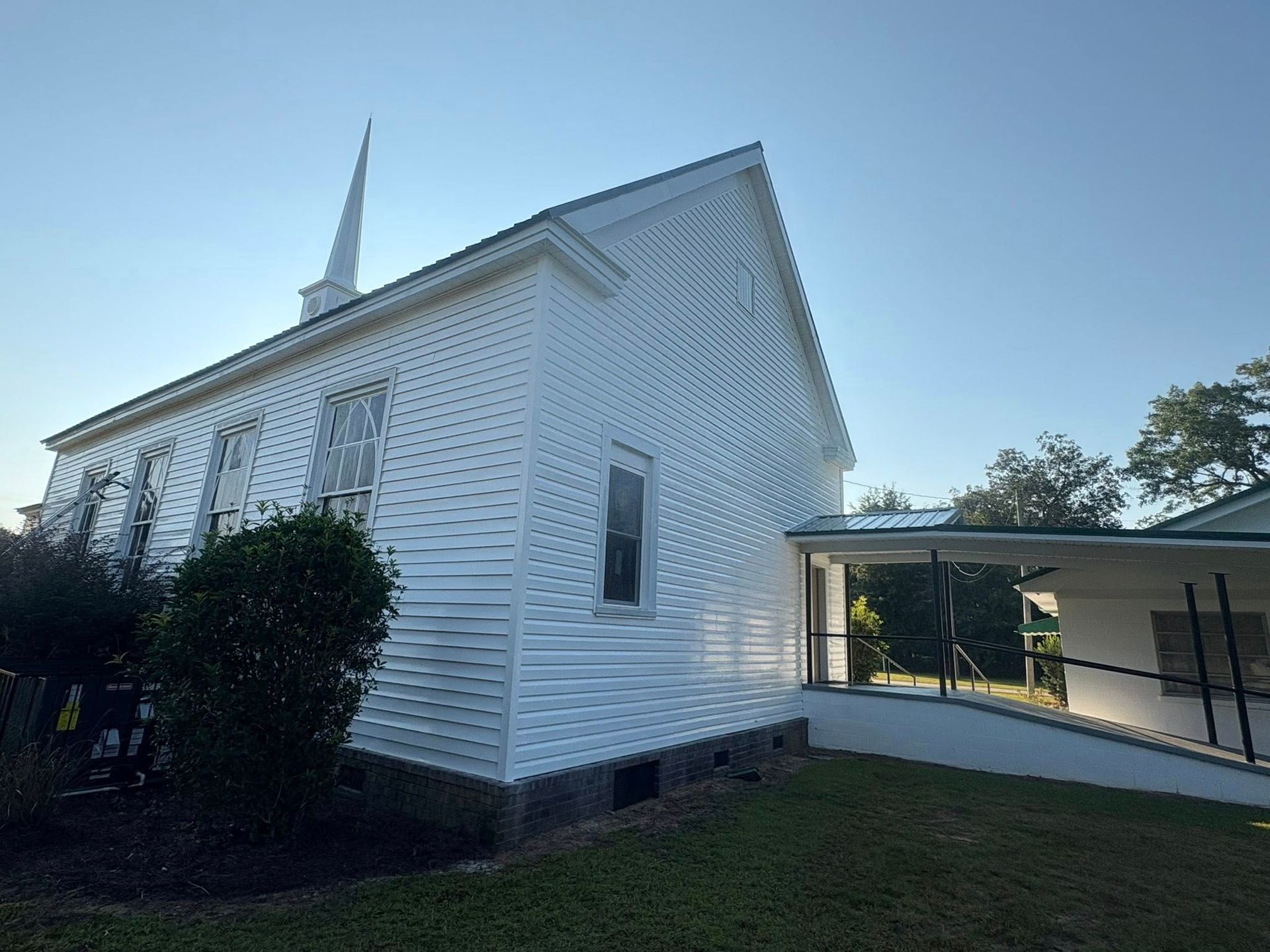 White wooden church with steeple, long windows, and a ramp for accessibility.