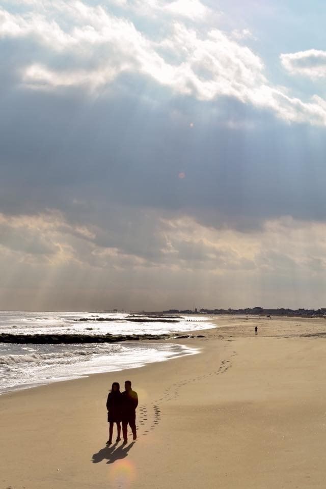 Two people standing on a beach looking at the ocean
