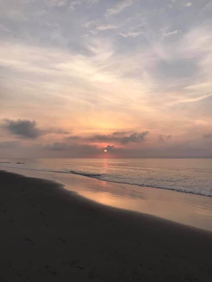 The sun is setting over the ocean on a beach.