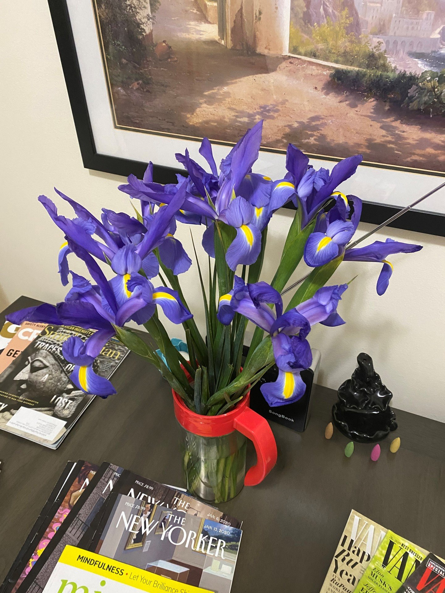 A vase of purple flowers sits on a table next to magazines